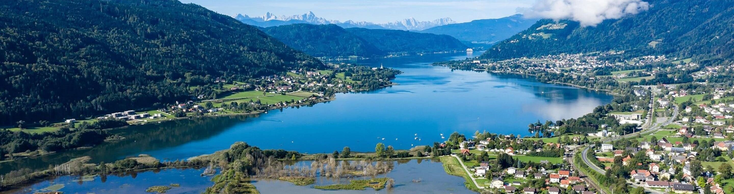 Ein Panoramablick auf einen See, umgeben von Bergen, einer kleinen Stadt und einem Kirchturm.