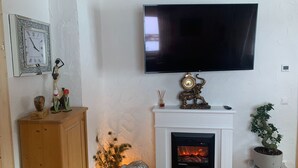 A living room with a fireplace, a mounted television, and decorative items including a clock and figurines.