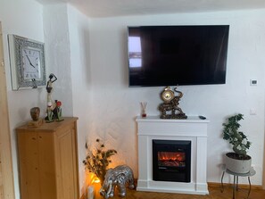 A living room with a fireplace, a mounted television, and decorative items including a clock and figurines. - Alpine Holiday Home in Lungau (Muhr)