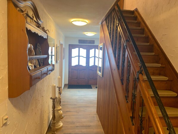 A wooden staircase leading to a door with a window, a wall-mounted shelf with decorative items, and a wall-mounted light fixture. - Alpine Holiday Home in Lungau (Muhr)