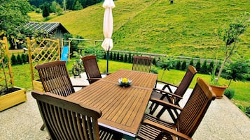 A wooden table and chairs on a patio with a view of a green hillside.