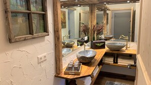 A bathroom with a rustic design, featuring a large mirror, wooden beams, and a stone basin sink.