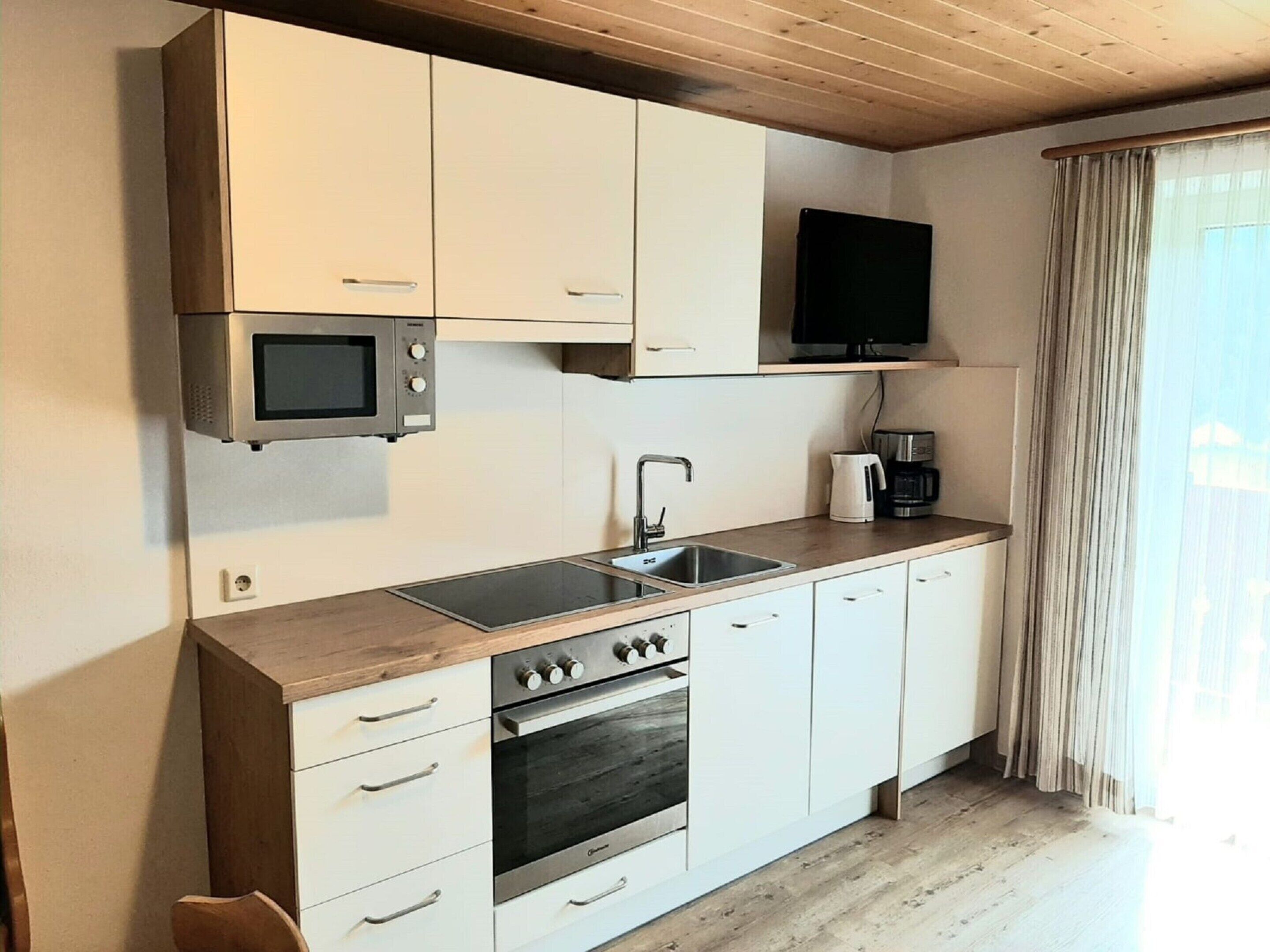 Una cocina moderna con gabinetes blancos, un microondas integrado, una estufa, un lavamanos y un televisor de pantalla plana.