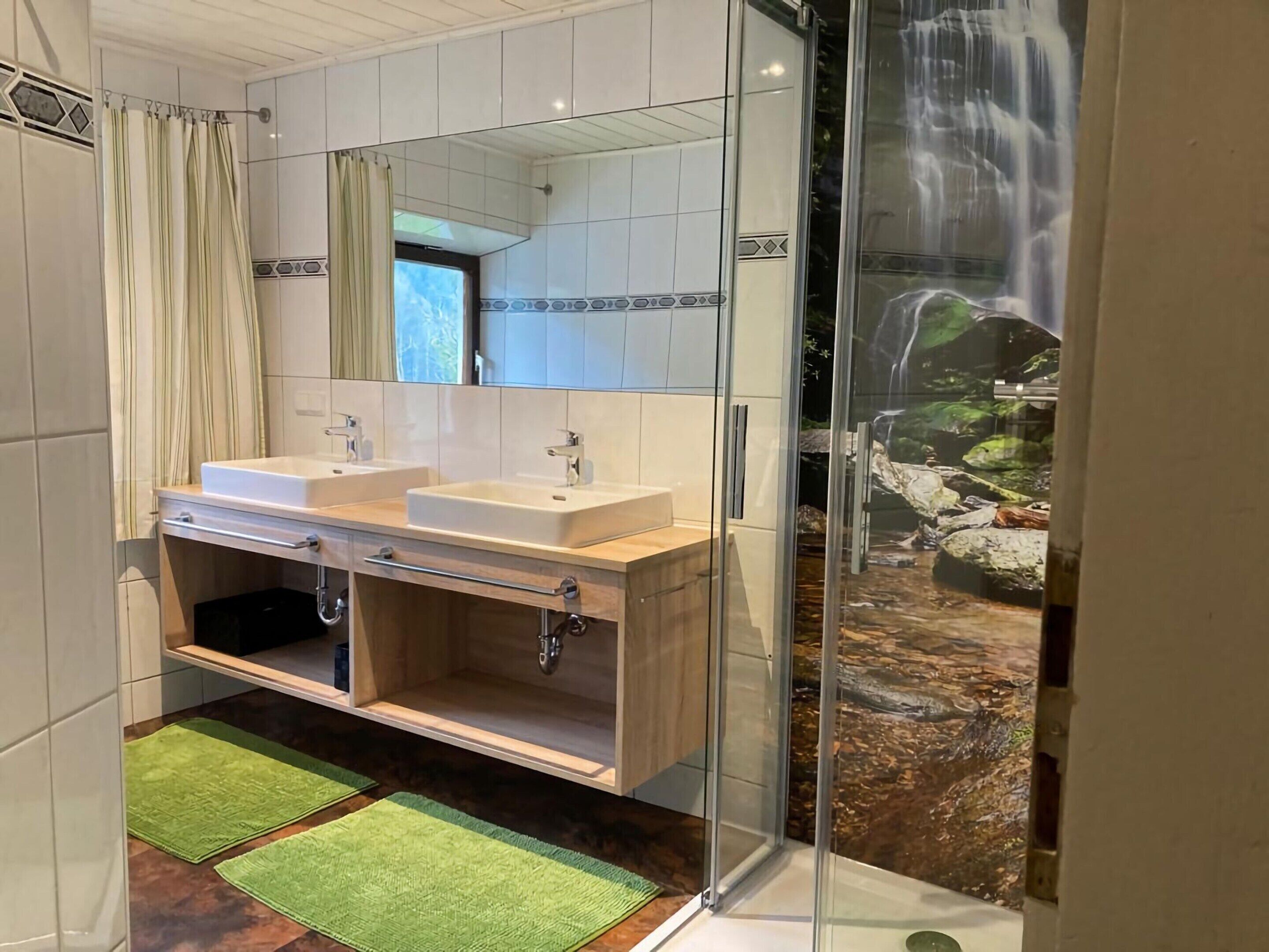 A bathroom with two sinks, a mirror, and a shower enclosure with a waterfall view.