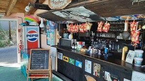 A bar area with a chalkboard menu, Pepsi refrigerator, and various snacks hanging above the counter. - Romantic Apartment in Mpenitses With Shared Pool (Corfu)