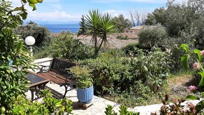 A patio with a bench and potted plants, overlooking a coastal landscape with trees and a view of the sea. - Romantic Apartment in Mpenitses With Shared Pool (Corfu)
