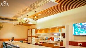 A modern bar area with a long counter, bar stools, and a television screen displaying a sports event. - HOTEL A9 BARNALA (Barnala)
