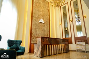 Zona de recepción con pared de mármol, mostrador de recepción, candelabro y sillón azul.
