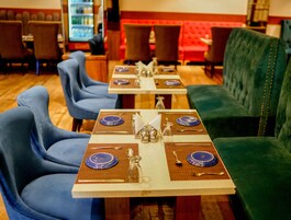 Un restaurante con sillas azules, sofás verdes y mesas dispuestas con platos, vasos y cubiertos.