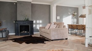 A modern living room with a fireplace, a sofa, a dining table with chairs, and a large window.