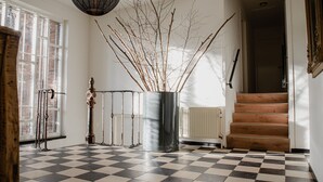 A checkered floor, a radiator, a staircase, and a vase with branches.