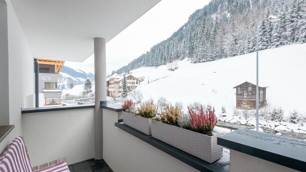Un balcone con vista su un paesaggio montano innevato, una baita di legno e un edificio con un'insegna che riporta la scritta "Hof".
