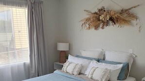 Une chambre à coucher avec un lit, une table de chevet, une lampe et une plante décorative.