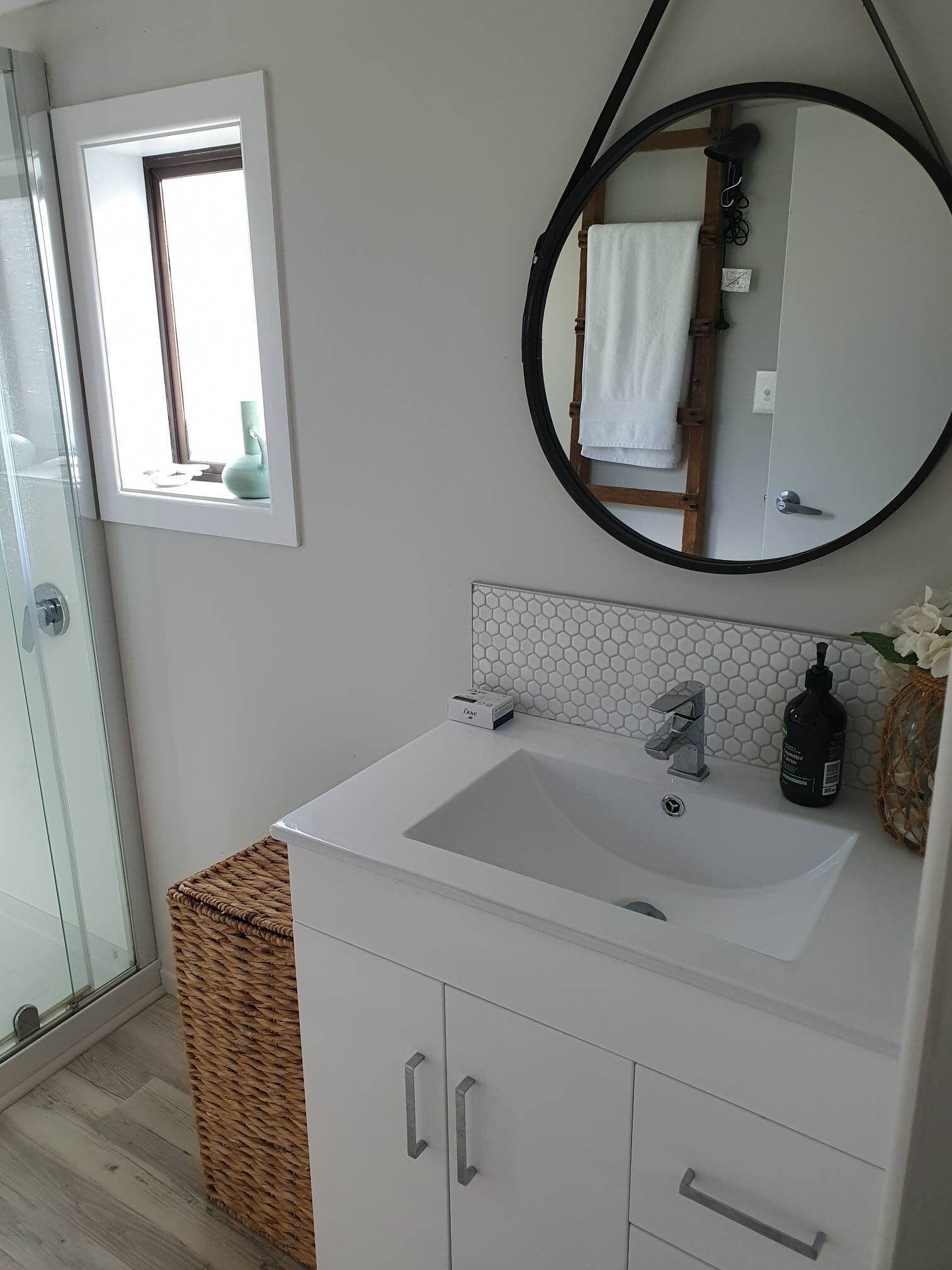 Une salle de bain avec un lavabo blanc, un miroir et une fenêtre.