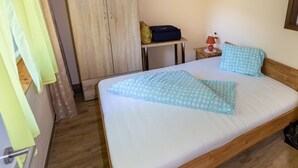 A hotel room with a bed, a wooden wardrobe, a small table with a lamp, and a suitcase. - Bungalow by Lake Ossiach With Mountain Views (Steindorf am Ossiacher See)