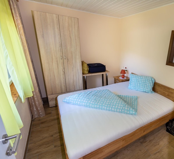 A hotel room with a bed, a wooden wardrobe, a small table with a lamp, and a suitcase. - Bungalow by Lake Ossiach With Mountain Views (Steindorf am Ossiacher See)