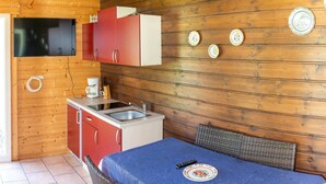 A compact kitchen with wooden walls, a red and white refrigerator, a coffee maker, and a sink. There is a table with a blue tablecloth and a plate, and wicker chairs. - Bungalow by Lake Ossiach With Mountain Views (Steindorf am Ossiacher See)