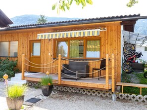 A wooden cabin with a covered porch, outdoor seating, and bicycles mounted on the wall. - Bungalow by Lake Ossiach With Mountain Views (Steindorf am Ossiacher See)