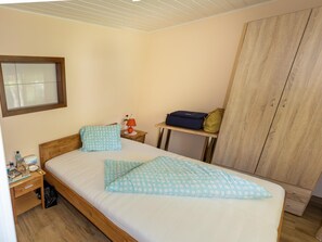 A bedroom with a wooden bed, a nightstand with a lamp, a small table with a bag, and a wardrobe. - Bungalow by Lake Ossiach With Mountain Views (Steindorf am Ossiacher See)
