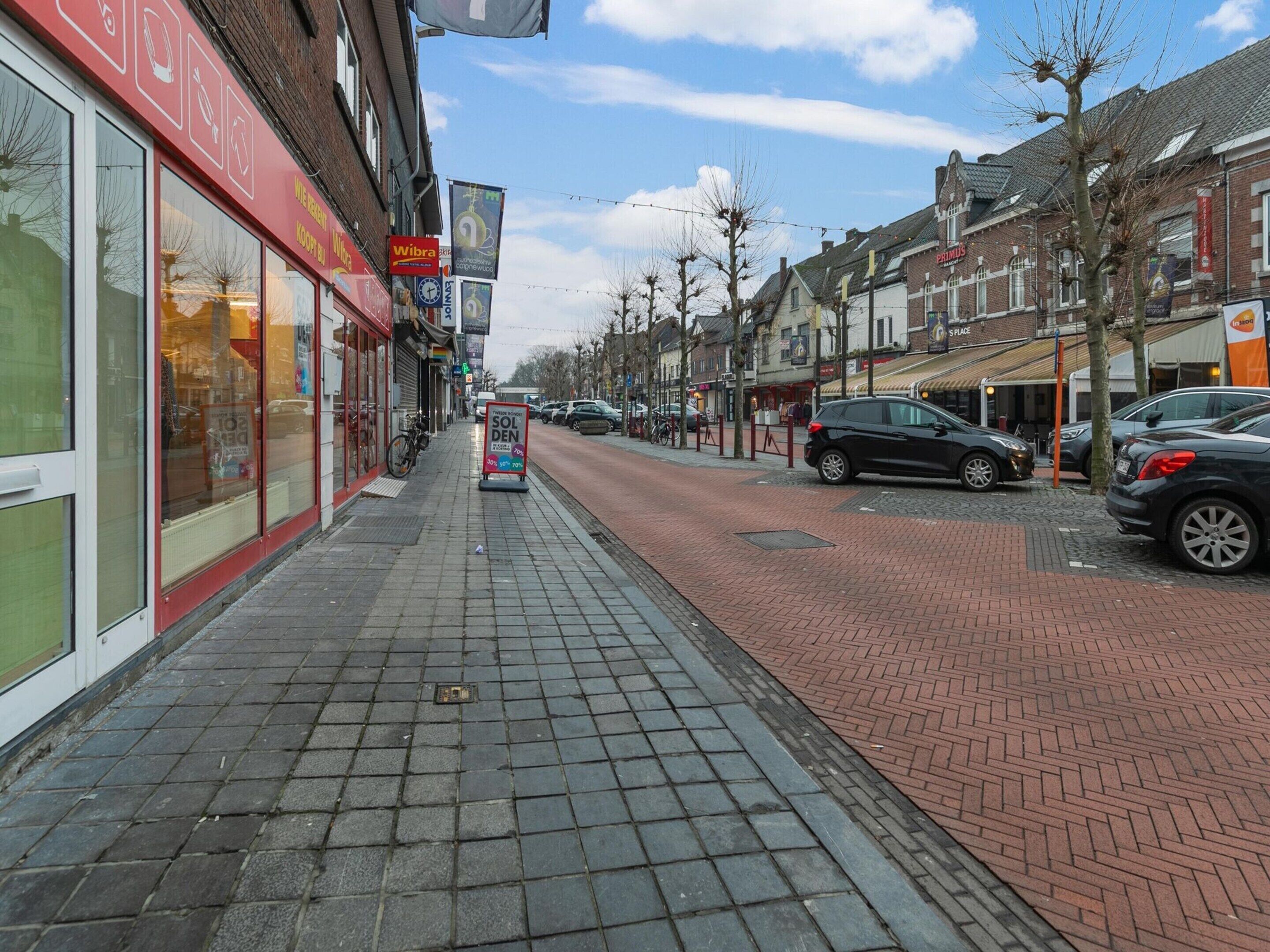 A street with shops, a signboard for 'Wibra', and parked cars.