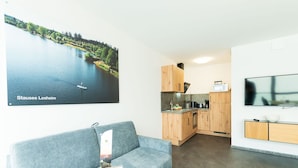 A modern living room with a grey sofa, a wooden coffee table, and a kitchen area with wooden cabinets and a flat-screen TV. - Modern Apartment in Mettlach With Infrared Sauna (Mettlach)