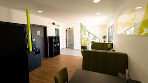 A modern hotel lobby with a reception desk, seating area, and a staircase leading to an upper floor. - Modern Apartment in Mettlach With Infrared Sauna (Mettlach)