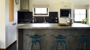 Een moderne keuken met een centraal eiland, barkrukken, een magnetron, een koffiezetapparaat en een klok aan de muur.