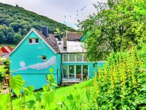 Una casa turquesa con un mural de piscina, rodeada de exuberante follaje y flores amarillas.