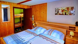 Una habitación de madera con literas, una cama con ropa de cama a rayas, una mesita de noche con una lámpara y un cuadro en la pared.