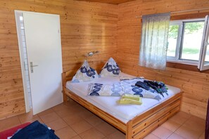 A wooden cabin room with a bed, a window with curtains, and a door.