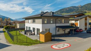 A modern building with a covered parking area, a fenced outdoor seating area, and a view of mountains in the background. - Holiday Home in Niedernsill Near ski Area (Niedernsill)