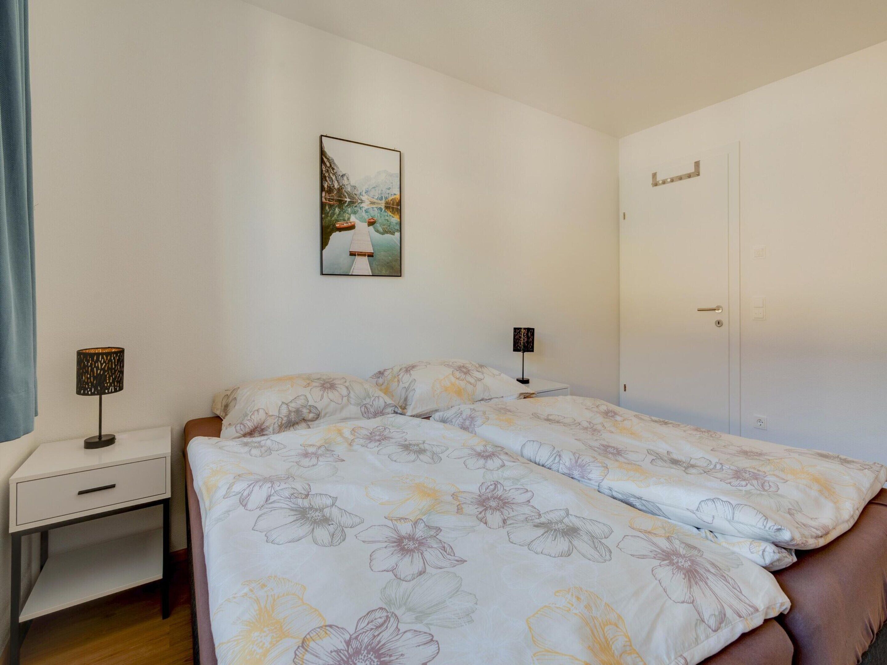 A bedroom with a bed, a desk, a chair, a lamp, and a door.