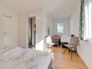 Une chambre à coucher avec un lit, deux chaises, une petite table et une fenêtre donnant sur des arbres.