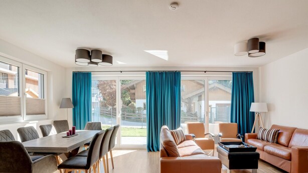 A spacious living area with a dining table, sofas, and a large window with curtains. - Holiday Home in Niedernsill Near ski Area (Niedernsill)