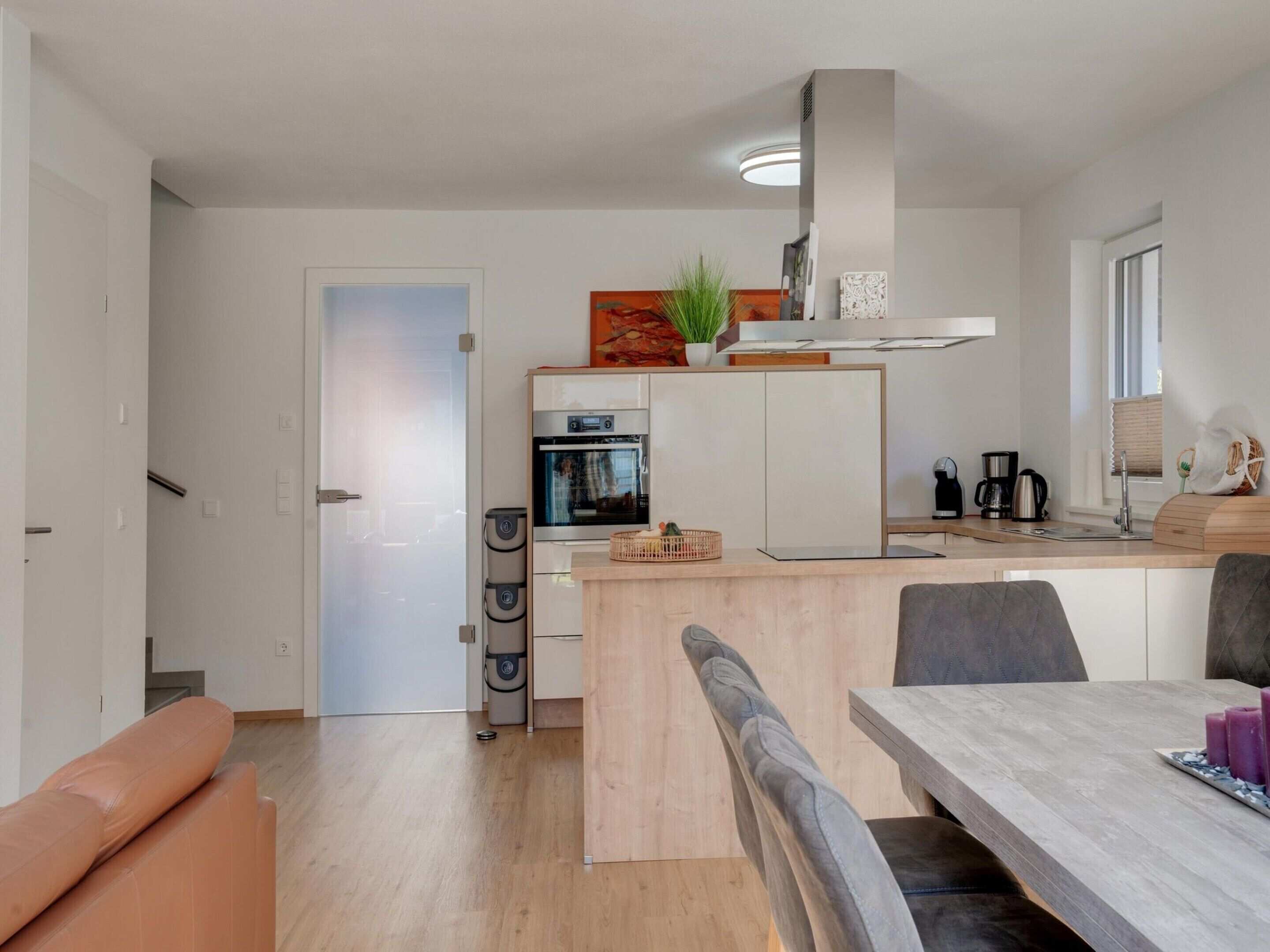 A modern kitchen with a built-in oven, a coffee machine, and a dining area with a wooden table and chairs.