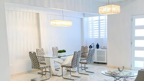Un espace de salle à manger moderne avec une table en verre et des chaises à motifs, un lustre et une vue sur une porte blanche.