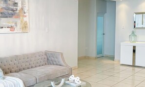 A living room with a sofa, a glass coffee table, and a painting on the wall. - Modern Chic House closed to the airport and beach (Carolina)
