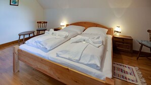 A wooden bed with white linens and towels, two bedside tables with lamps, a chair, and a patterned rug on a wooden floor. - Apartment in Mooswald in Carinthia With Pool (Fresach)