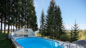 A swimming pool with a glass enclosure, surrounded by tall trees and a clear sky. - Apartment in Mooswald in Carinthia With Pool (Fresach)