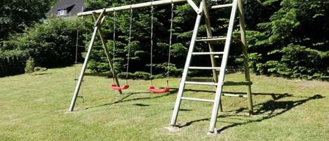 A swing set with a ladder in a grassy yard with trees in the background.