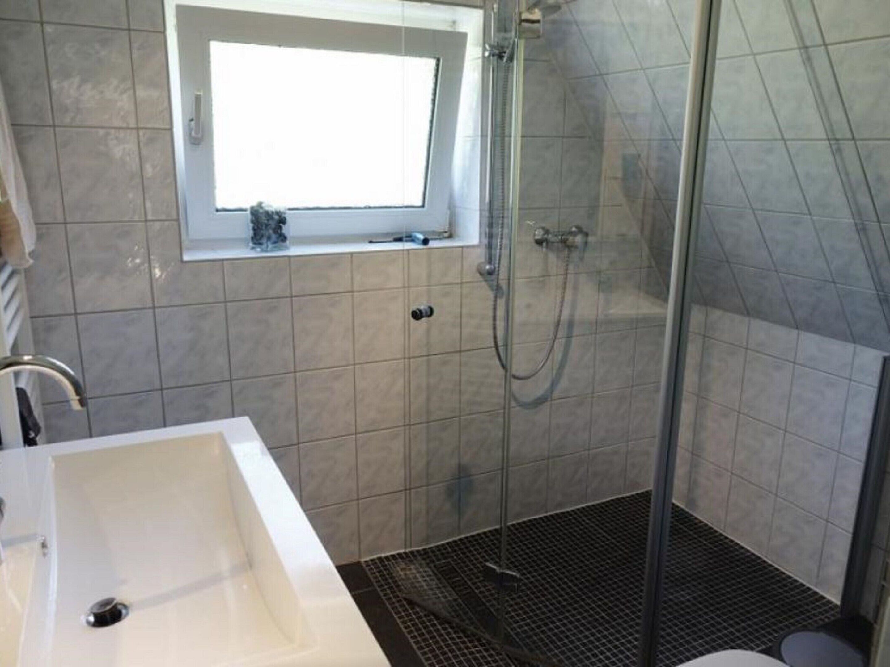 Ein Badezimmer mit Dusche, Waschbecken und Fenster.