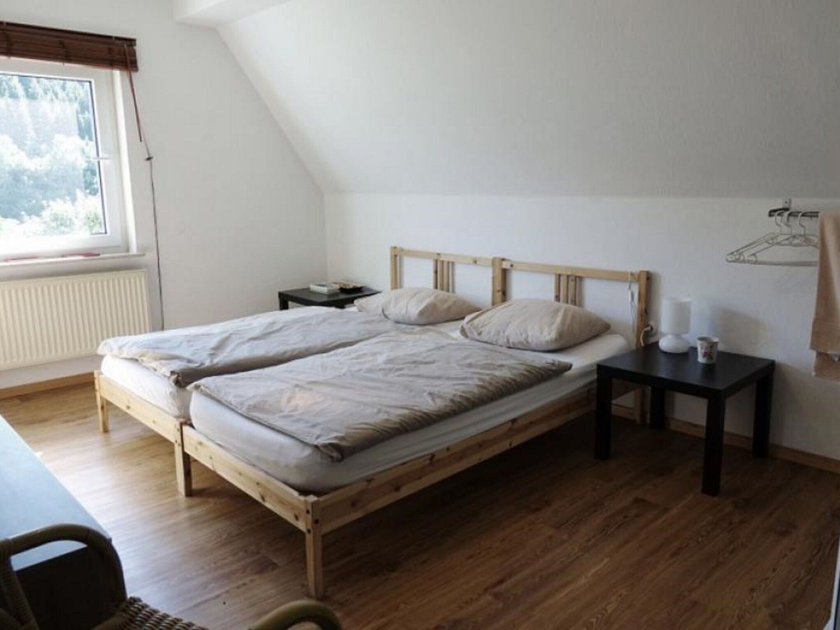 Ein Schlafzimmer mit einem hölzernen Bett, einem Nachttisch, einem Fenster mit Jalousien und einer Heizung.