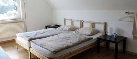 Ein Schlafzimmer mit einem hölzernen Bett, einem Nachttisch, einem Fenster mit Jalousien und einer Heizung.