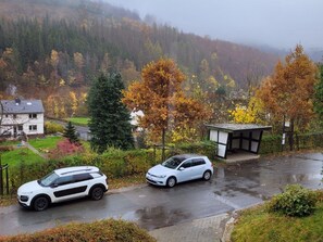 A residential area with two parked cars, a house, and a small building with a sloped roof. - Holiday Home With Terrace in Sauerland (Brilon)