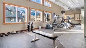Un gimnasio con equipamiento de ejercicio, ventanas amplias y un banco.