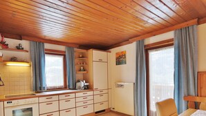 A kitchen with wooden cabinets, a built-in oven, and a dining area with a table and chairs. - Ferienwohnung mit Herrlicher Terrasse & Fun+ Card (Niedernsill)