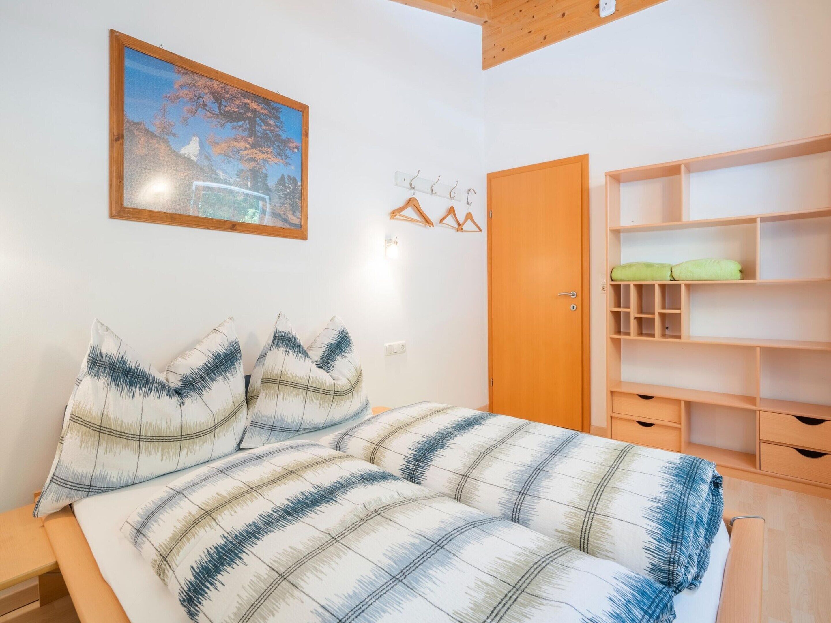 A bedroom with a bed, a wooden wardrobe, and a painting on the wall.
