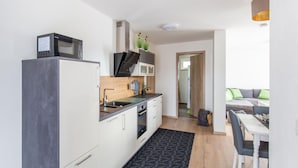 Een kleine keuken met een magnetron, fornuis en wastafel. Er is een zithoek met een tafel en stoelen.