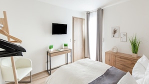 Een moderne slaapkamer met een bed, een bureau, een stoel, een televisie en een kledingkast.