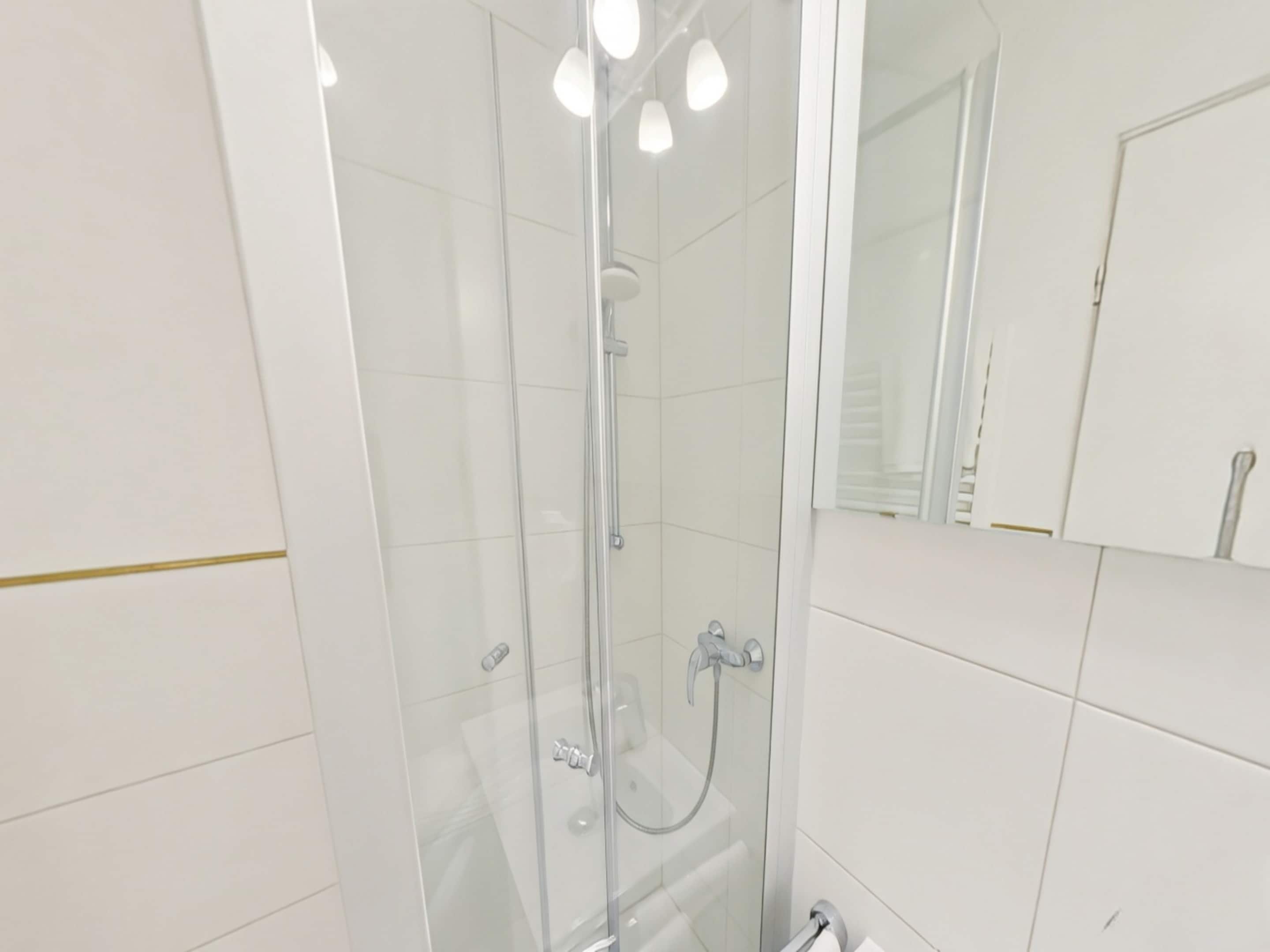 Ein modernes Badezimmer mit einer Duschkabine aus Glas, einem Spiegel und weiß gefliesten Wänden.